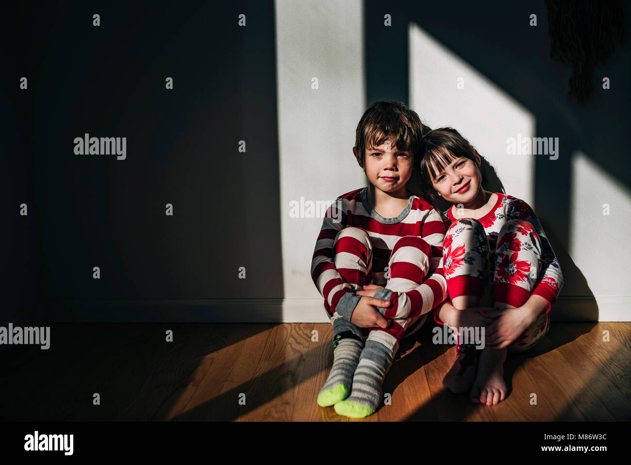 Un ragazzo e una ragazza in pigiama seduto sul pavimento bagnato dal sole Foto Stock