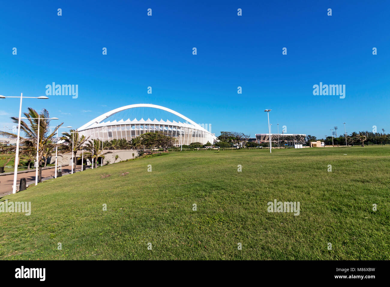 DURBAN, Sud Africa - Febbraio 2018: la mattina presto erba vuoto lwn area ricreativa contro Mosè Mabhida Stadium e cielo blu a Durban, Sud Afri Foto Stock