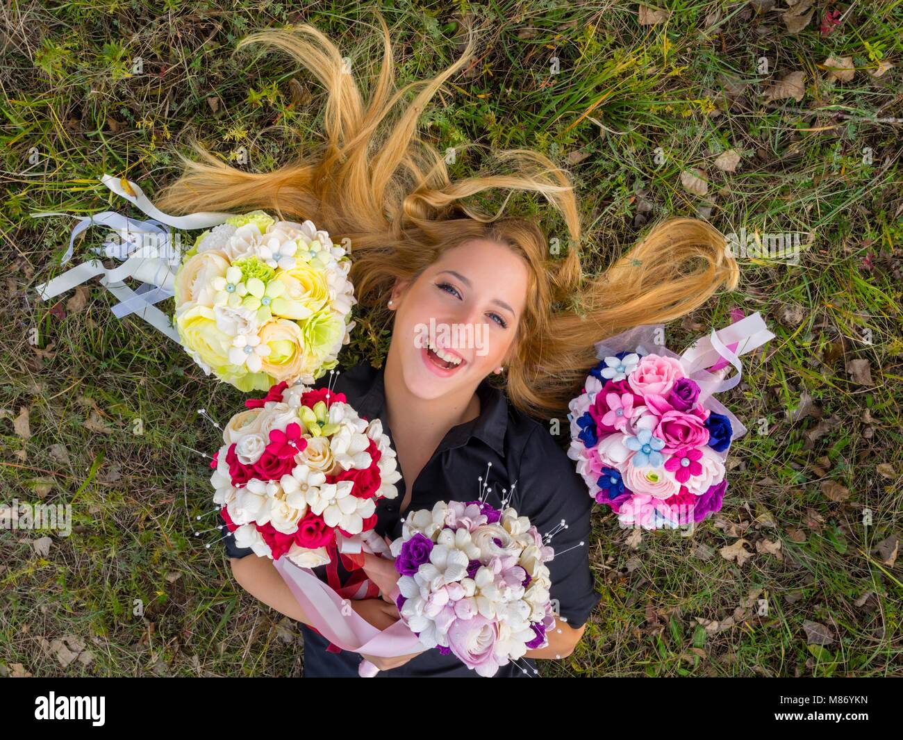 Blonde capelli sparsi sorridente felice ridendo ritratto headshot adolescente steso sulla sua schiena tra colorati fiori bouquet Foto Stock