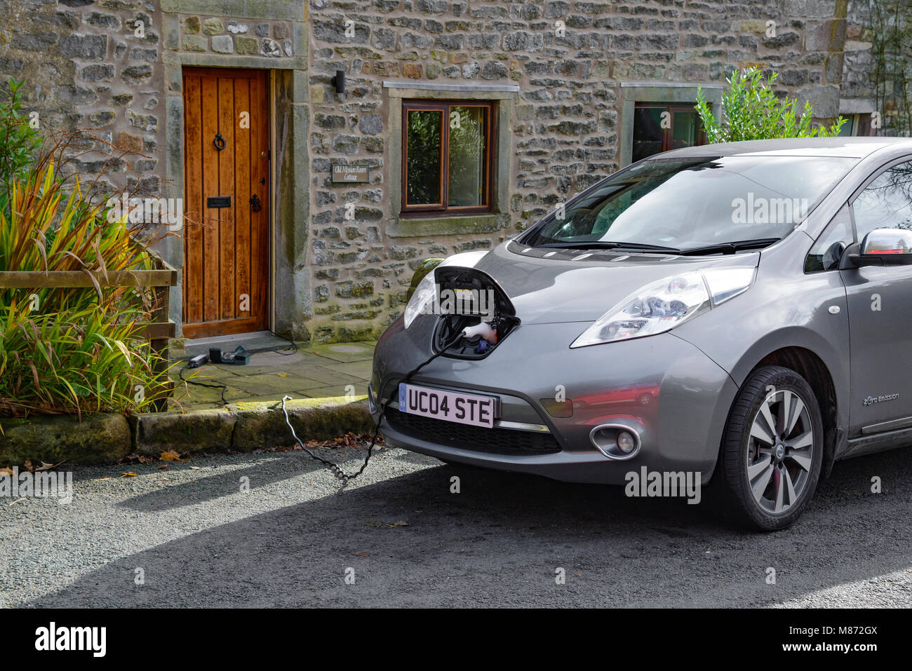 Una Nissan Leaf auto elettrica essendo addebitato al di fuori di un cottage, Newton, Clitheroe, Lancashire, Regno Unito. Foto Stock