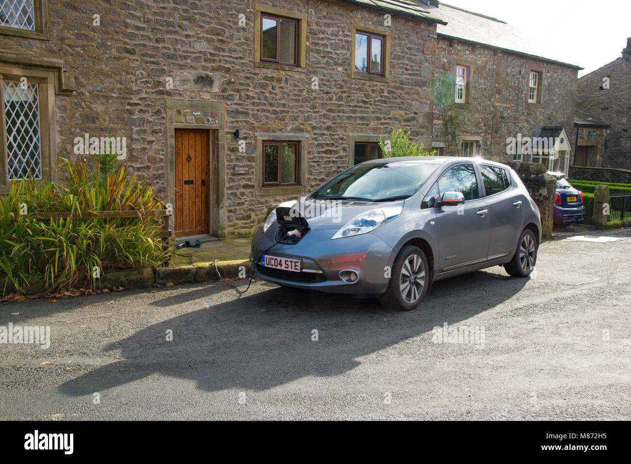 Una Nissan Leaf auto elettrica essendo addebitato al di fuori di un cottage, Newton, Clitheroe, Lancashire, Regno Unito. Foto Stock