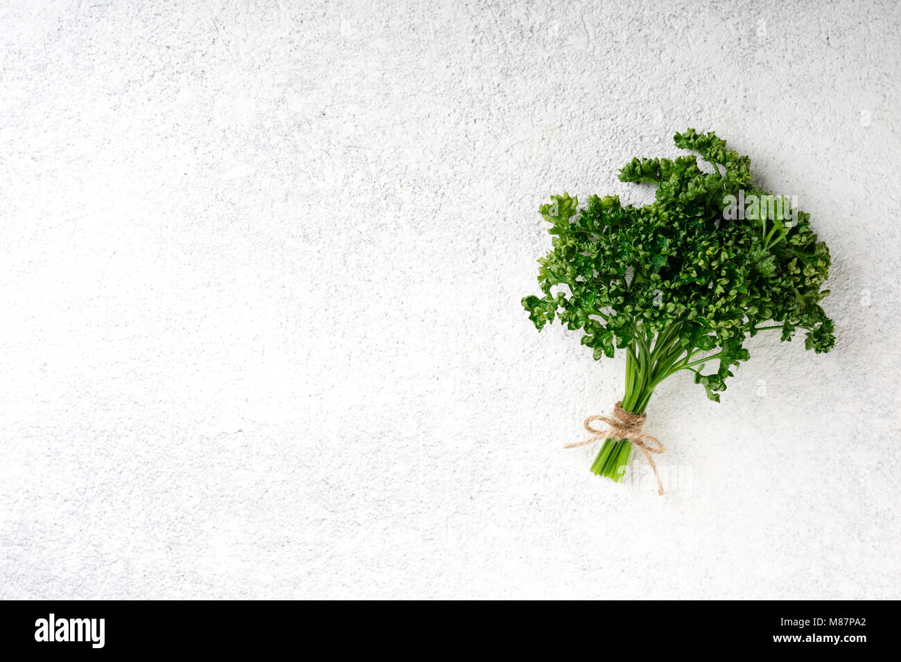 Mazzetto di prezzemolo sul cemento bianco sullo sfondo. Prezzemolo fresco alle erbe. Cibo vegetariano sfondo, vista dall'alto. Spazio di copia Foto Stock