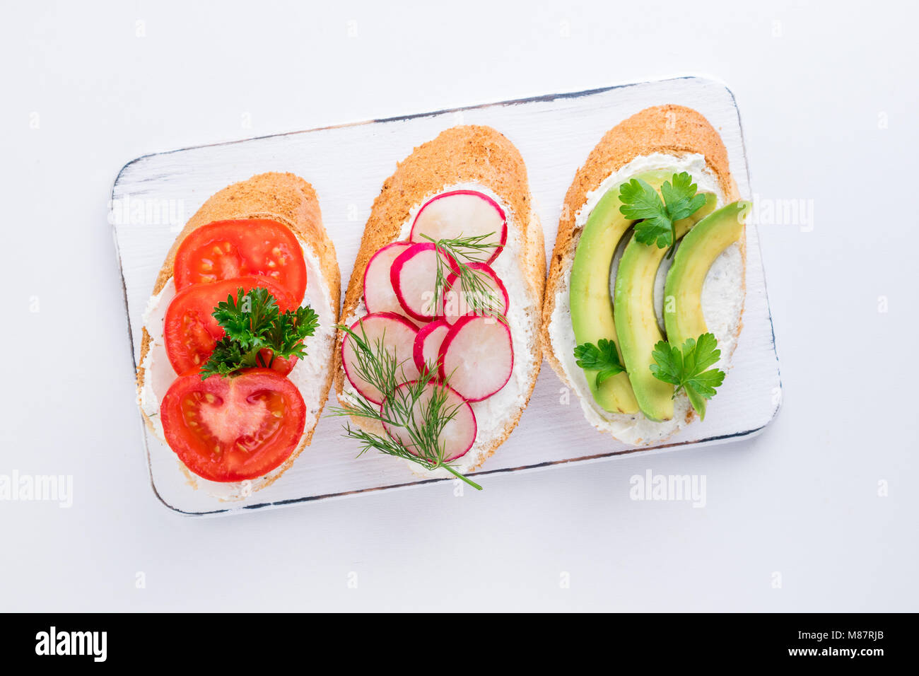 Mini sandwich con crema di formaggio, verdure e avocado. Varietà di panini su sfondo bianco, vista dall'alto. Lay piatto Foto Stock