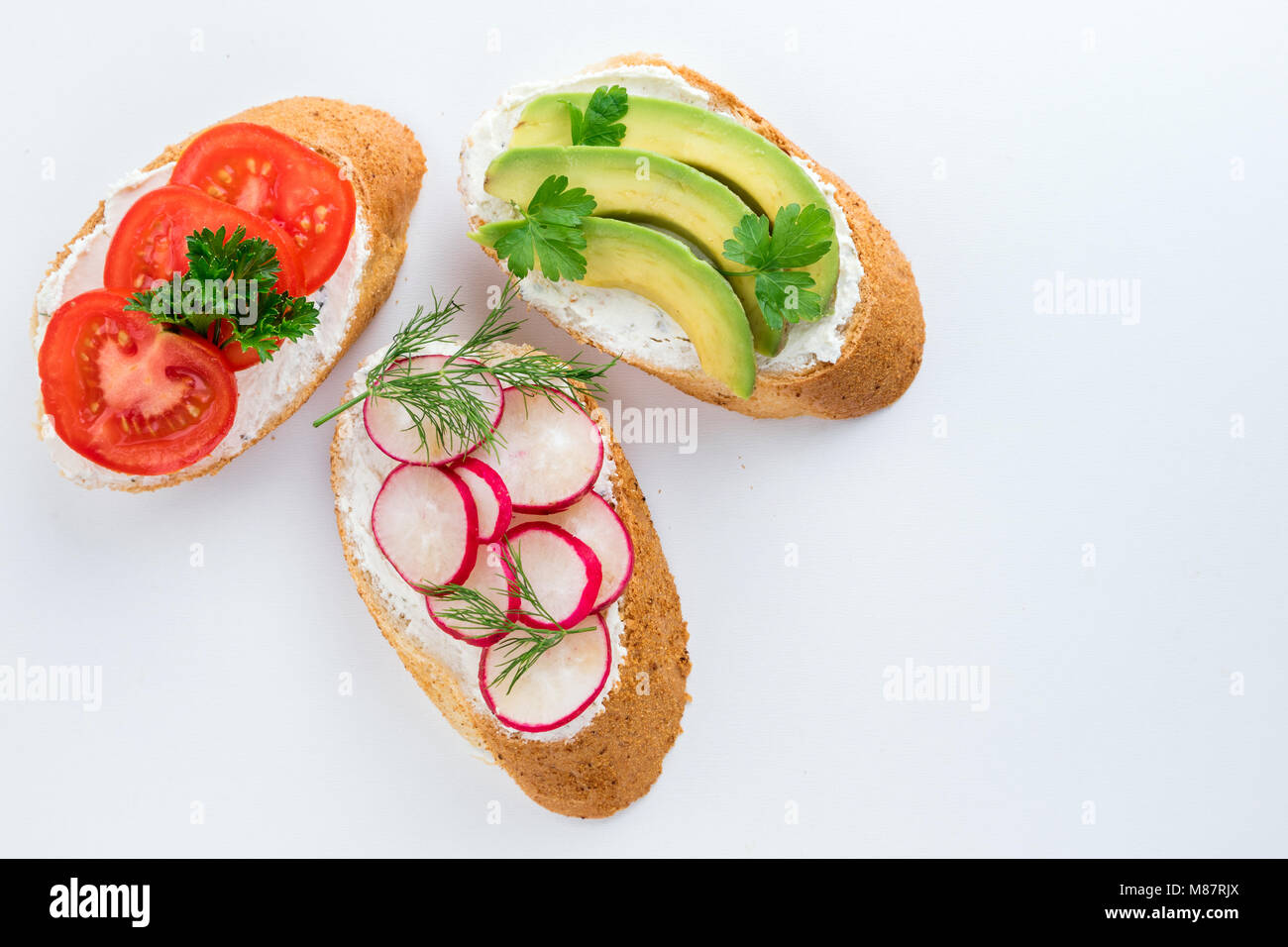 Mini sandwich con crema di formaggio, verdure e avocado. Varietà di panini su sfondo bianco, vista dall'alto. Lay piatto Foto Stock