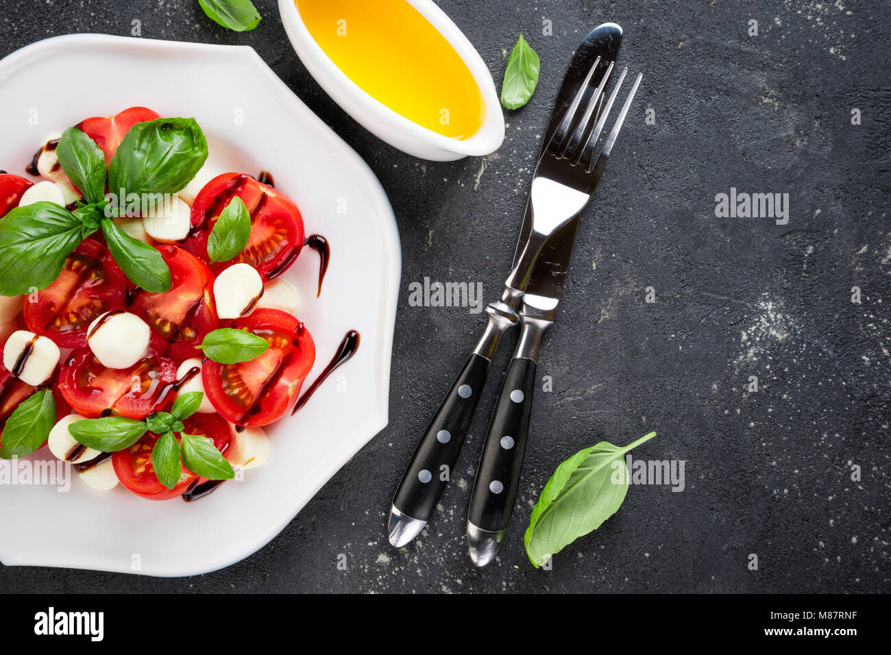 Insalata caprese. Il formaggio mozzarella, pomodoro, olio d'oliva e basilico foglie di erbe su sfondo di calcestruzzo. Mangiare sano vegetali cibo vegetariano Foto Stock