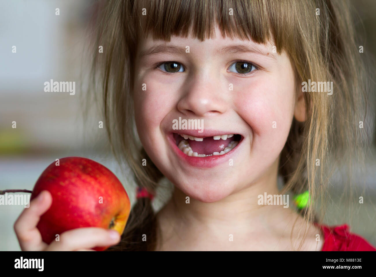 Un Grazioso Piccolo Ricci Ragazza Sdentati Sorrisi E Mantiene Una Mela Rossa Ritratto Di Un Bambino Felice Di Mangiare Una Mela Rossa Il Bambino Perde I Denti Di Latte Cibo Sano Foto