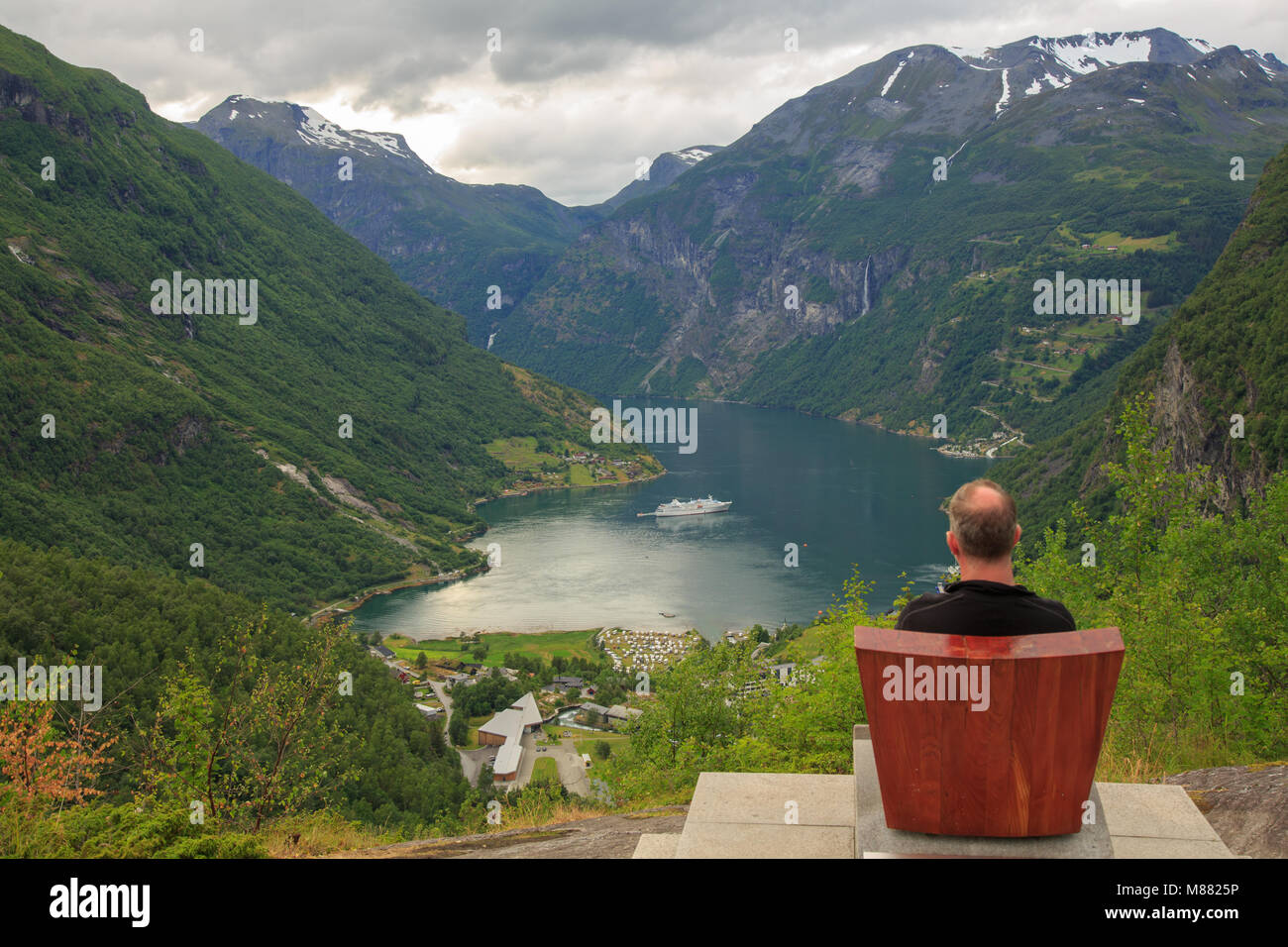 L'uomo guarda la vista dal Belvedere Flydalsjuvet in Geiranger - Il Geirangerfjord, villaggio di Geiranger e una nave da crociera che lascia il porto Foto Stock