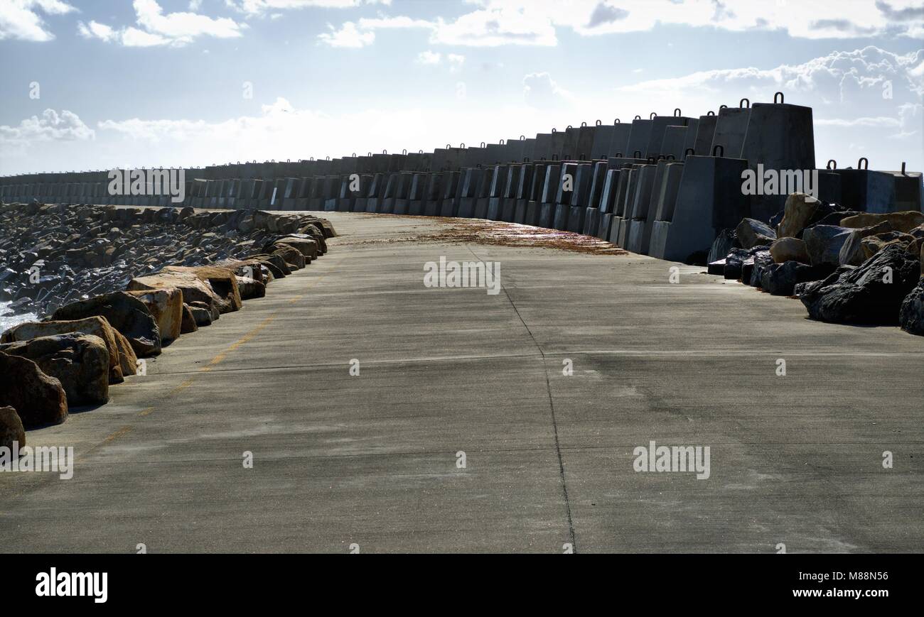 Percorso di calcestruzzo del punto Corambirra frangiflutti in Coffs Harbour, Nuovo Galles del Sud, Australia. Immagine ha Breakwall, grandi massi, rocce, sky Foto Stock