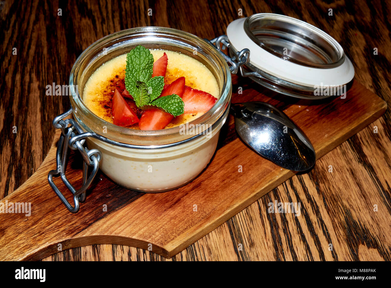 Crema dessert brulle in vetro e metallo vaso con una fragola e menta topping sul legno marrone scuro dello sfondo della tabella Foto Stock