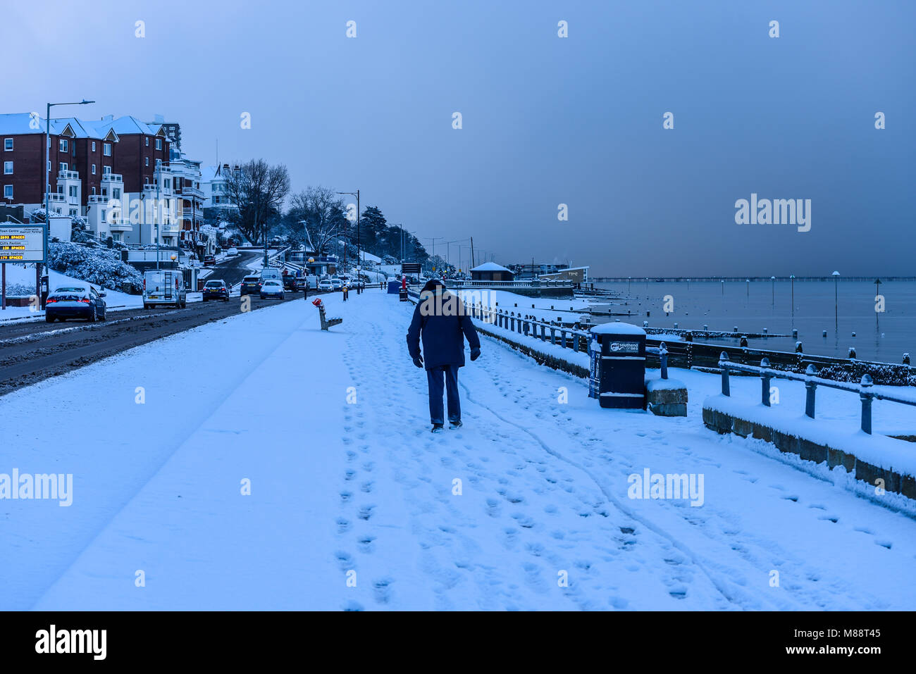 Uomo con attenzione a piedi nella neve lungo Southend on Sea seafront, Essex, estuario del Tamigi. La mattina presto di bestia da est meteo fenomeno Foto Stock