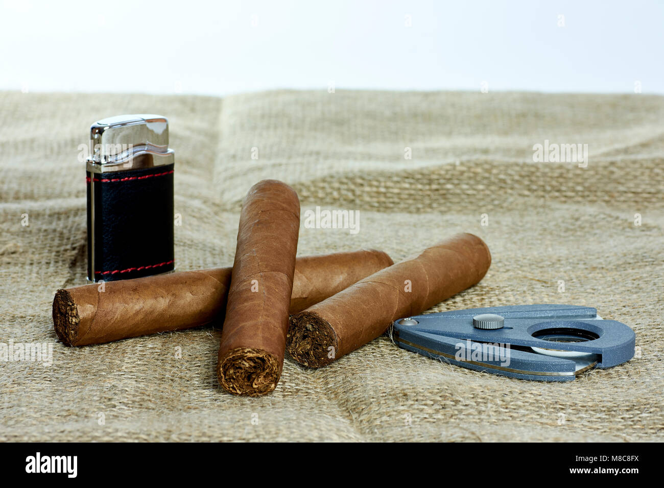 Tre sigari cubani con una taglierina e un accendino su sfondo bianco Foto Stock