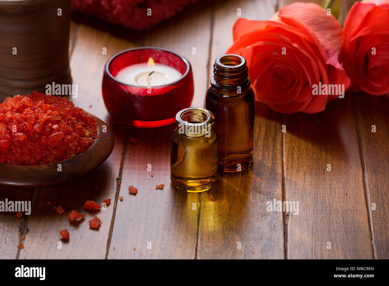 Olio essenziale di minerali, sali da bagno, candela e fiori su il marrone del tavolo di legno. Foto Stock