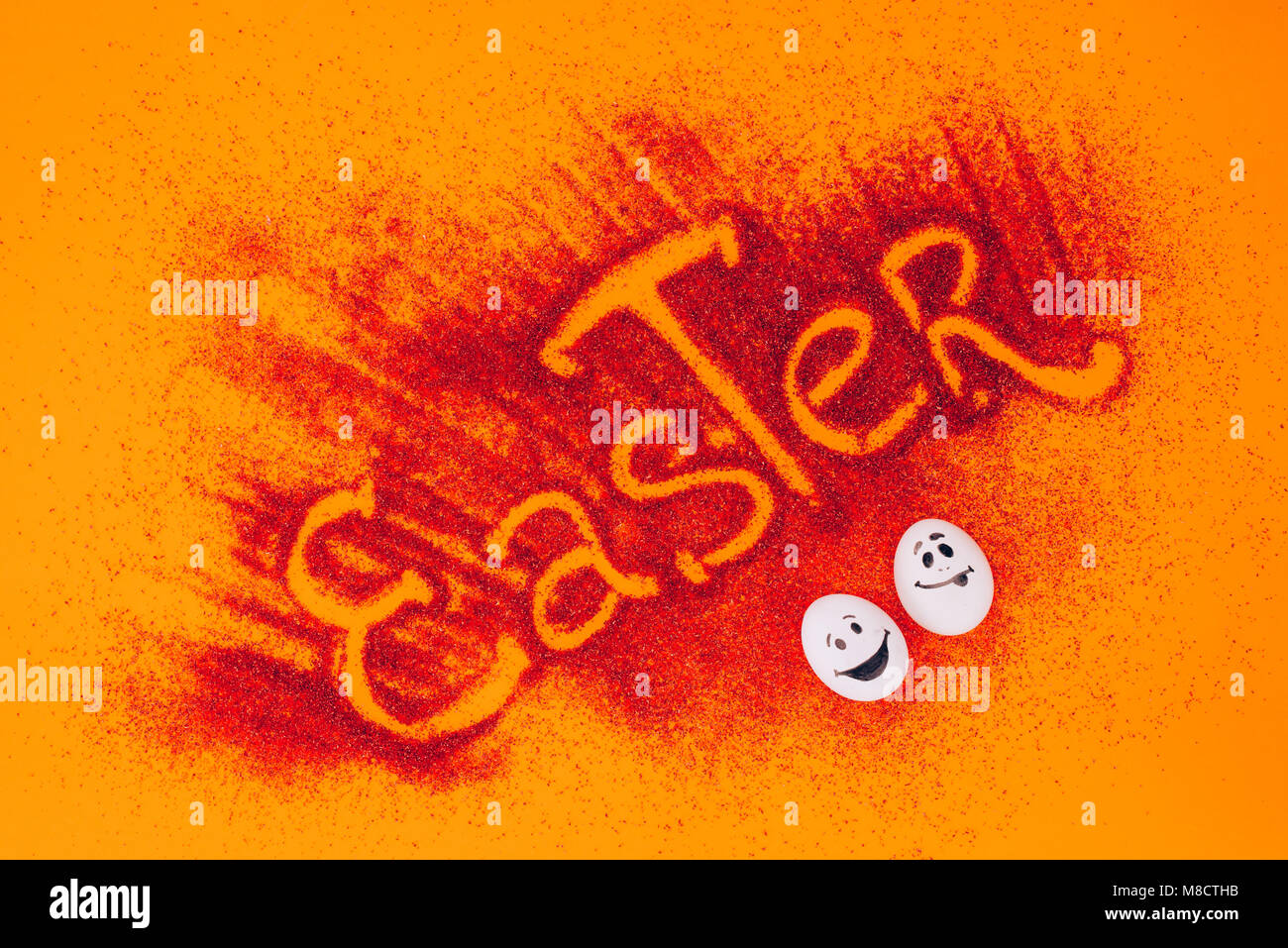Vista superiore del segno di pasqua fatta di sabbia rossa con uova di gallina con le faccine su Orange Foto Stock