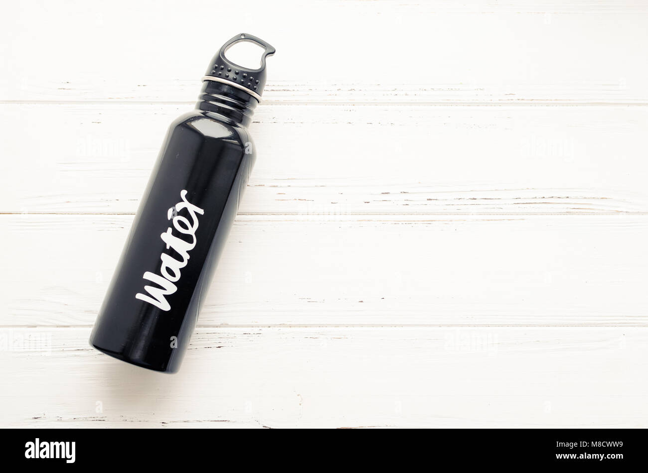 Alluminio nero acqua riutilizzabile bottiglia su bianco shabby chic sfondo di legno con posto per il testo. Bere più concetto. Vista dall'alto. Copia dello spazio. Foto Stock