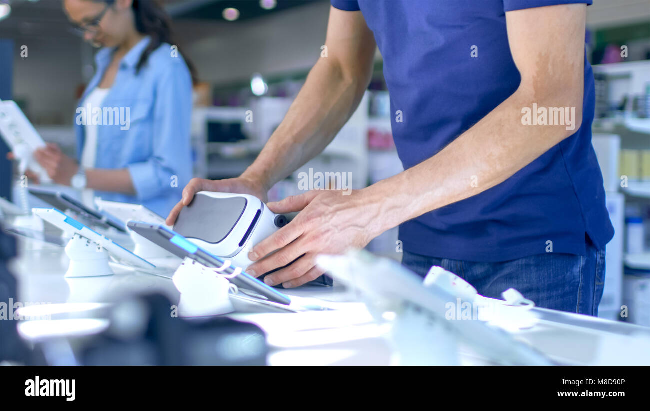 Nel negozio di elettronica giovane uomo è tenuto in Realtà Virtuale auricolare. Egli è nel moderno, luminoso negozio che ha tutti i dispositivi più recenti. Foto Stock