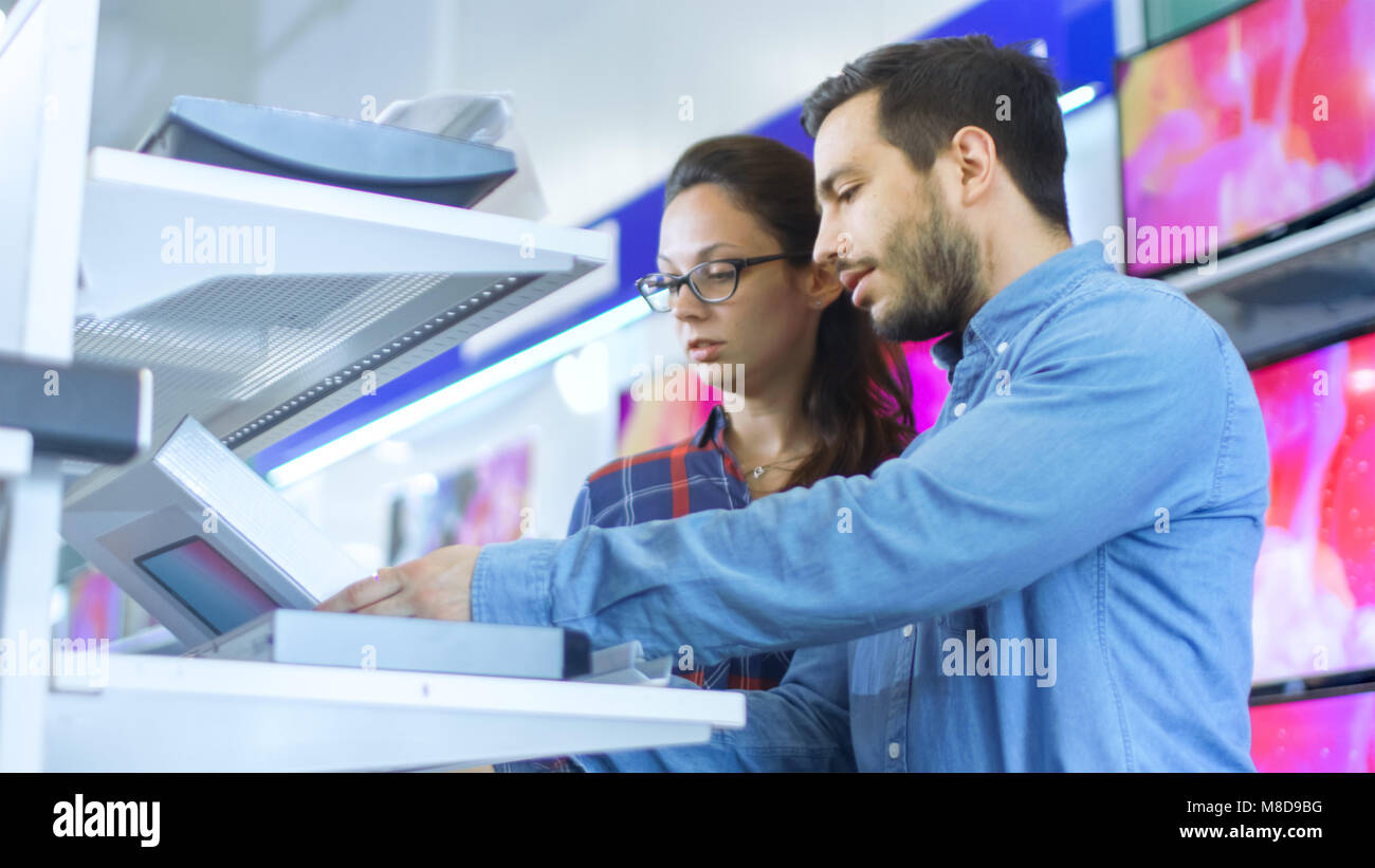 Bella coppia Giovane nel negozio di elettronica la navigazione, cercando nuovi gadget, compresse e foto/videocamere presentato sui ripiani. Foto Stock