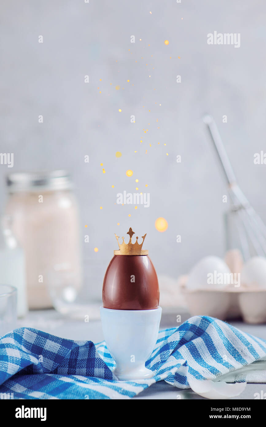 Il cioccolato uovo di pasqua con corona d'oro e la caduta di glitter in una cocotte di porcellana. Elevato La chiave dello sfondo con copia spazio. Il pagamento di royalty e di concetto di unicità Foto Stock