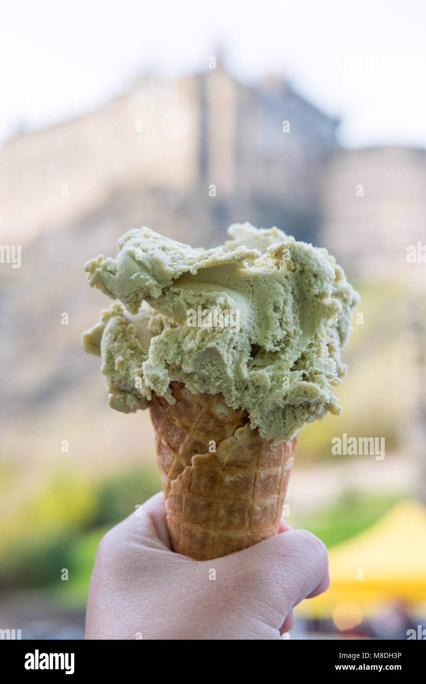 Mano che regge il gelato di pistacchio, gelato con blur sullo sfondo del Castello di Edimburgo. Foto Stock