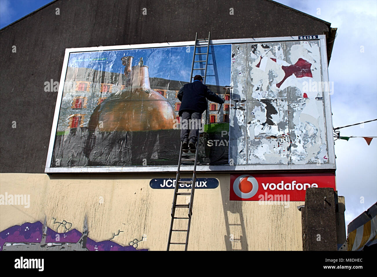 L'uomo una scaletta mettendo su un nuovo cartellone pubblicitario, affissioni di whisky jamesons un famoso whisky irlandese marca. skibbereen, Irlanda Foto Stock
