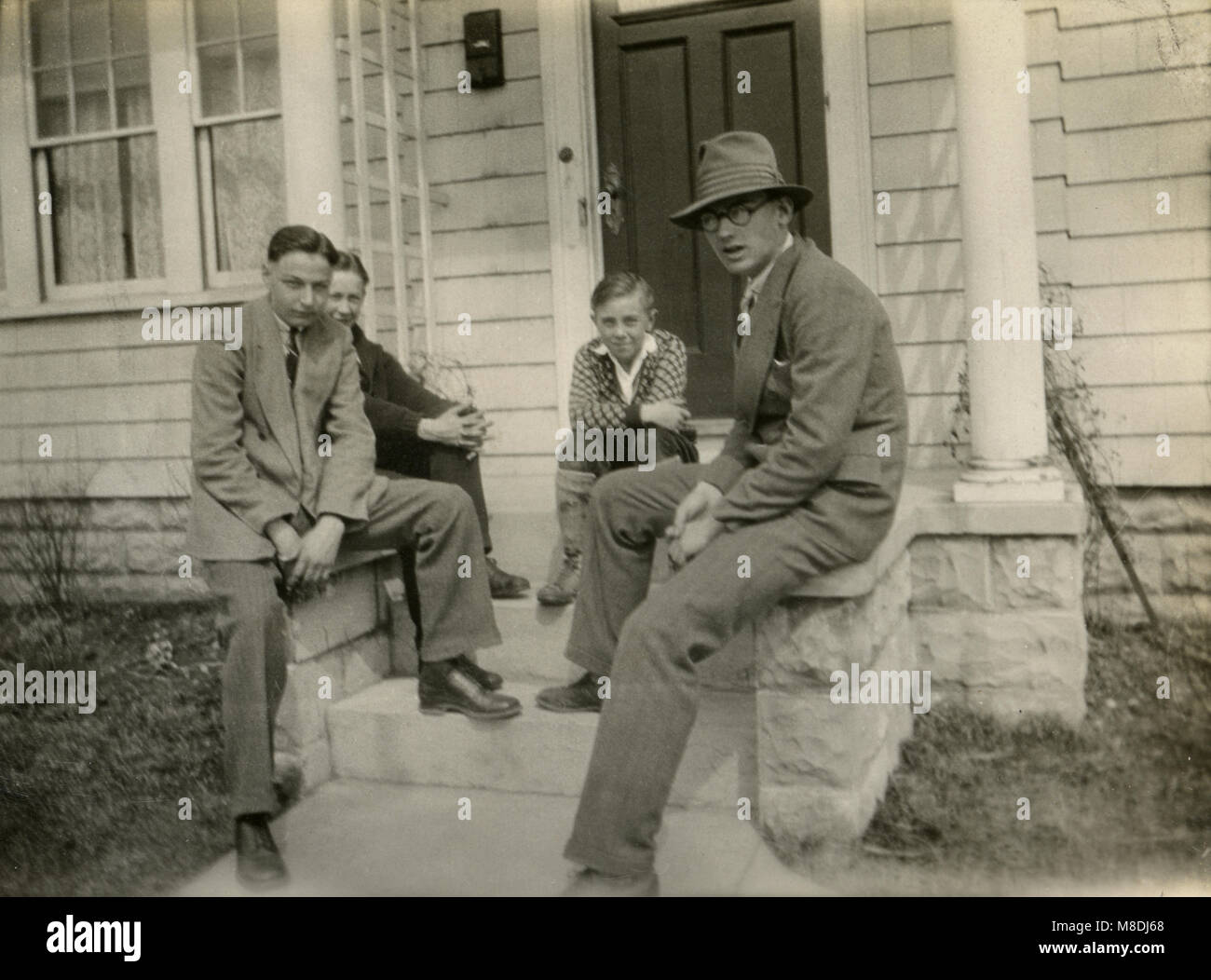 Antique c1920 fotografia, padre e tre ragazzi sedersi sulla parte anteriore passi di casa. Posizione sconosciuta, STATI UNITI D'AMERICA. Fonte: fotografia originale. Foto Stock