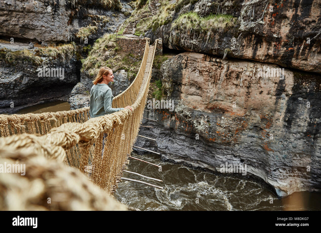 Turista femminile guardando fuori da Inca ponte di corde, Huinchiri, Cusco, Perù Foto Stock