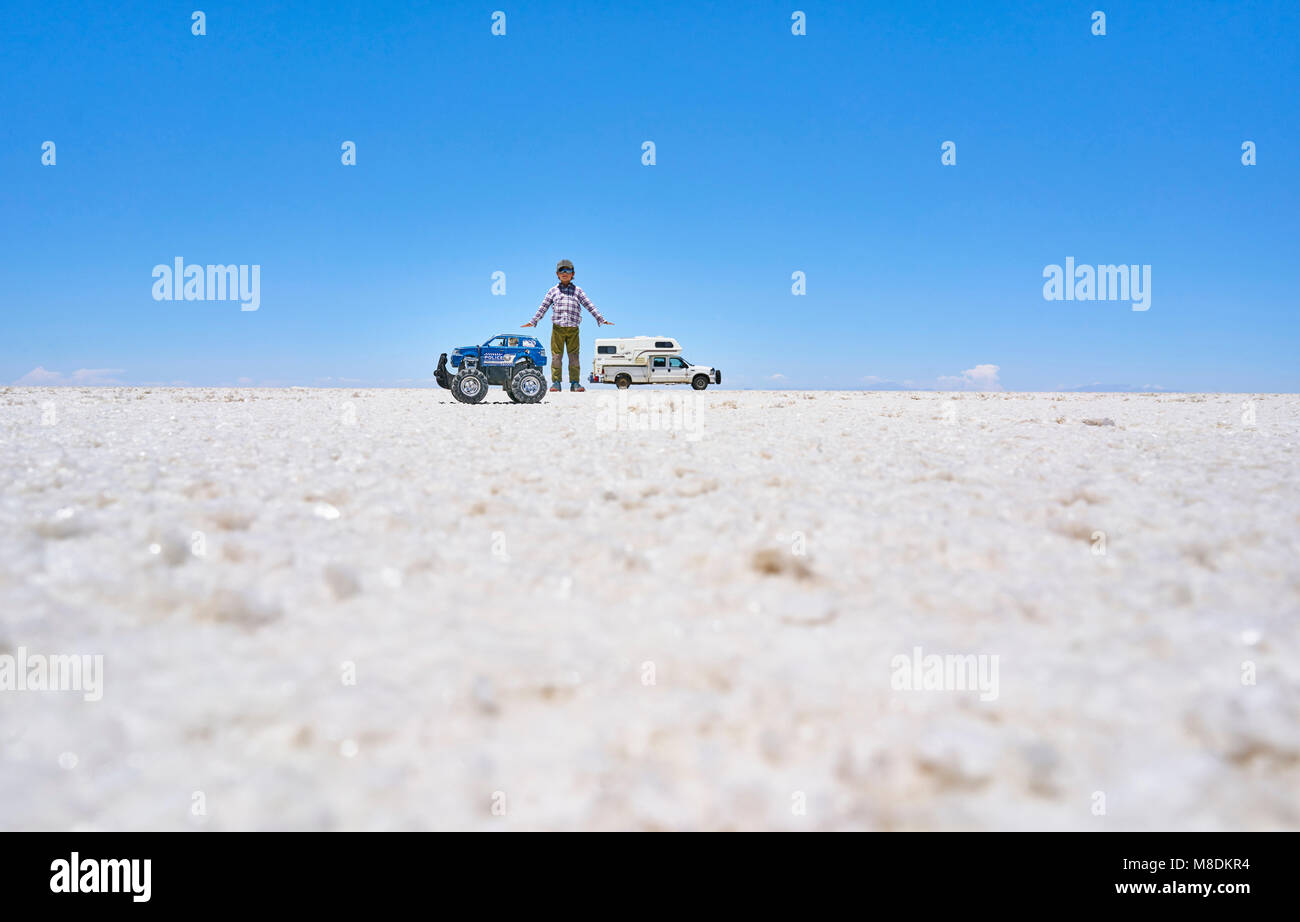 Falsa immagine in prospettiva del ragazzo e toy carrello su saline, in piedi alti più di veicolo in background, Salar de Uyuni, Bolivia Foto Stock