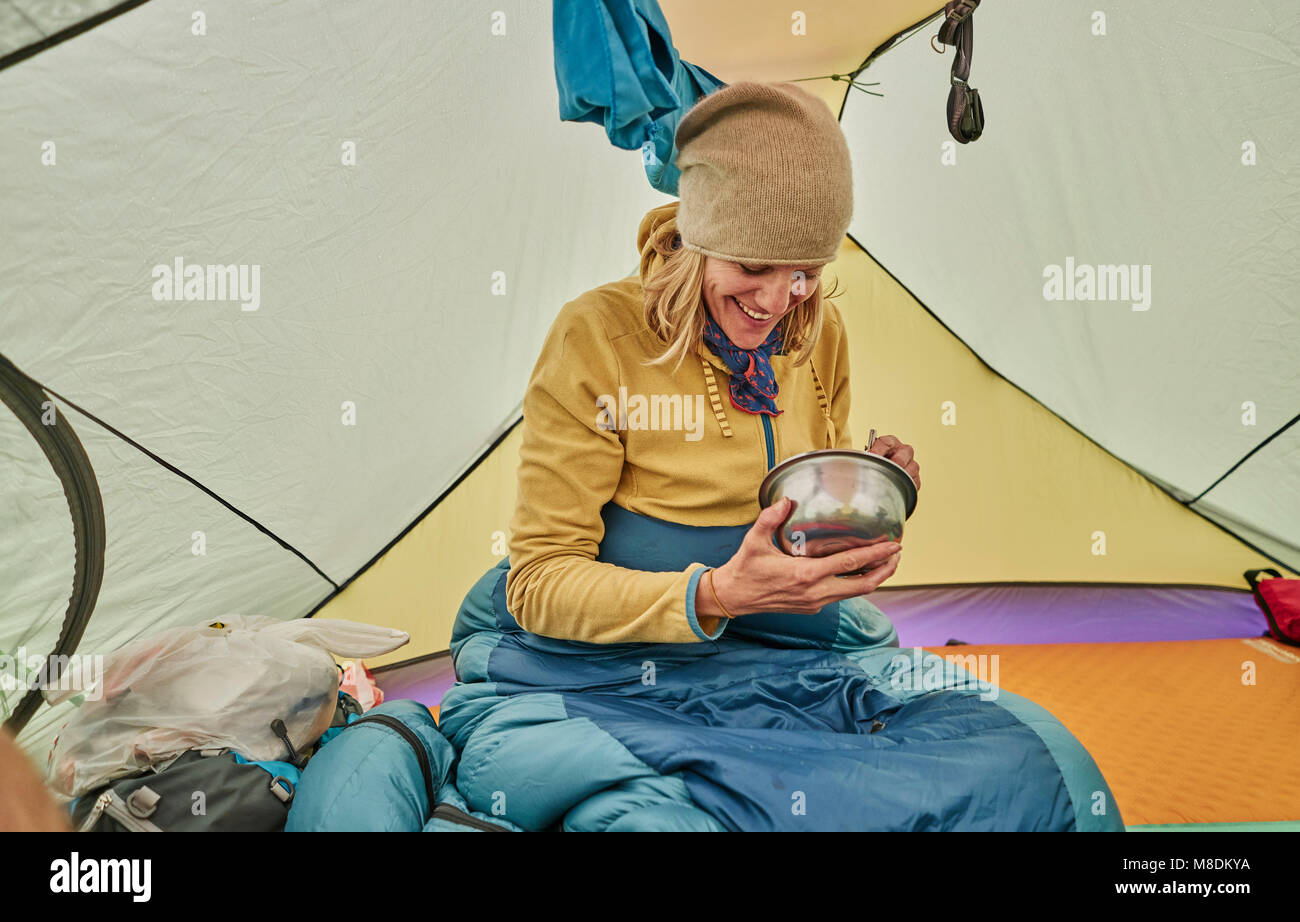 Donna seduta nella tenda a mangiare cibo dalla ciotola, Ventilla, La Paz, Bolivia, Sud America Foto Stock