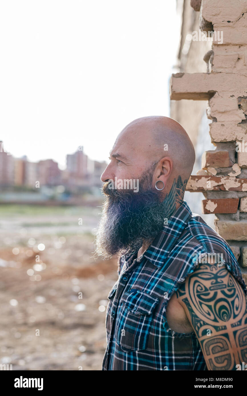 Tatuato maschio maturo hipster dalla parete di edificio demolito Foto Stock