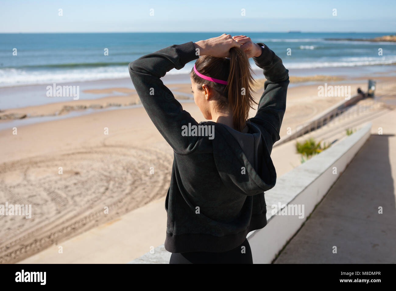 Vista posteriore del giovane donna alla spiaggia di capelli di legatura in coda di cavallo, Carcavelos, Lisboa, Portogallo, Europa Foto Stock