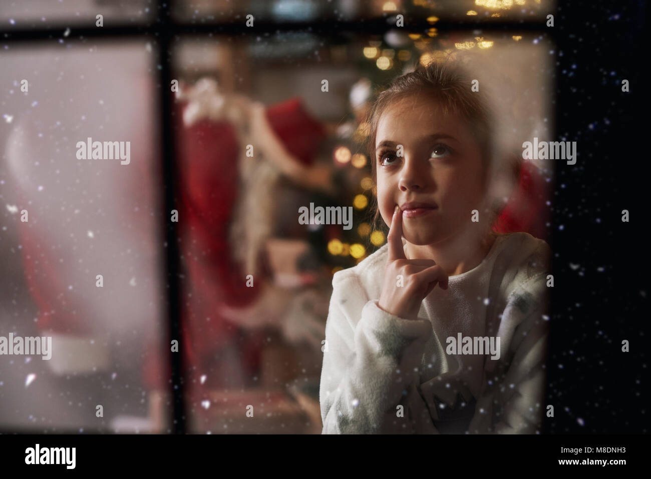 Ragazza giovane guardando fuori della finestra alla vigilia di Natale, Santa in background lasciando doni accanto a tree Foto Stock