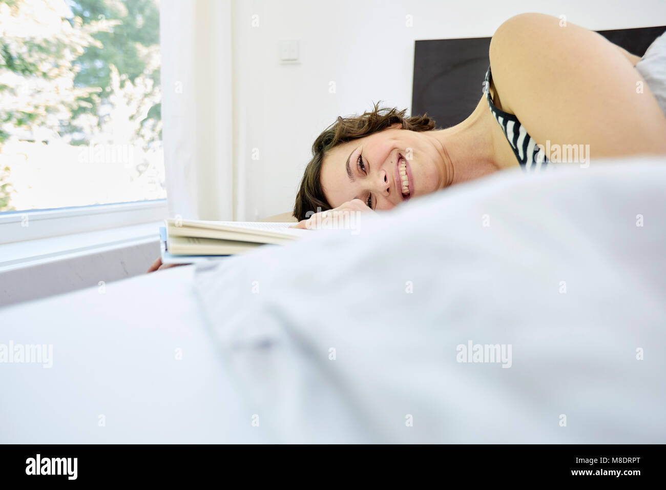 Metà donna adulta, rilassante sul letto, azienda prenota, sorridente Foto Stock