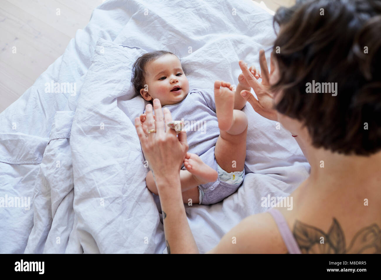 Baby girl giacente sul letto, madre cercando su di lei, riproduzione Foto Stock