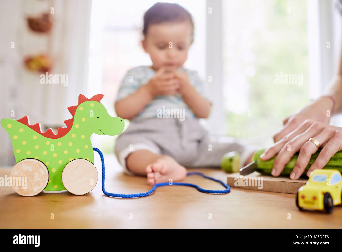 Baby ragazza seduta sul banco di cucina guarda la madre per affettare cetrioli Foto Stock