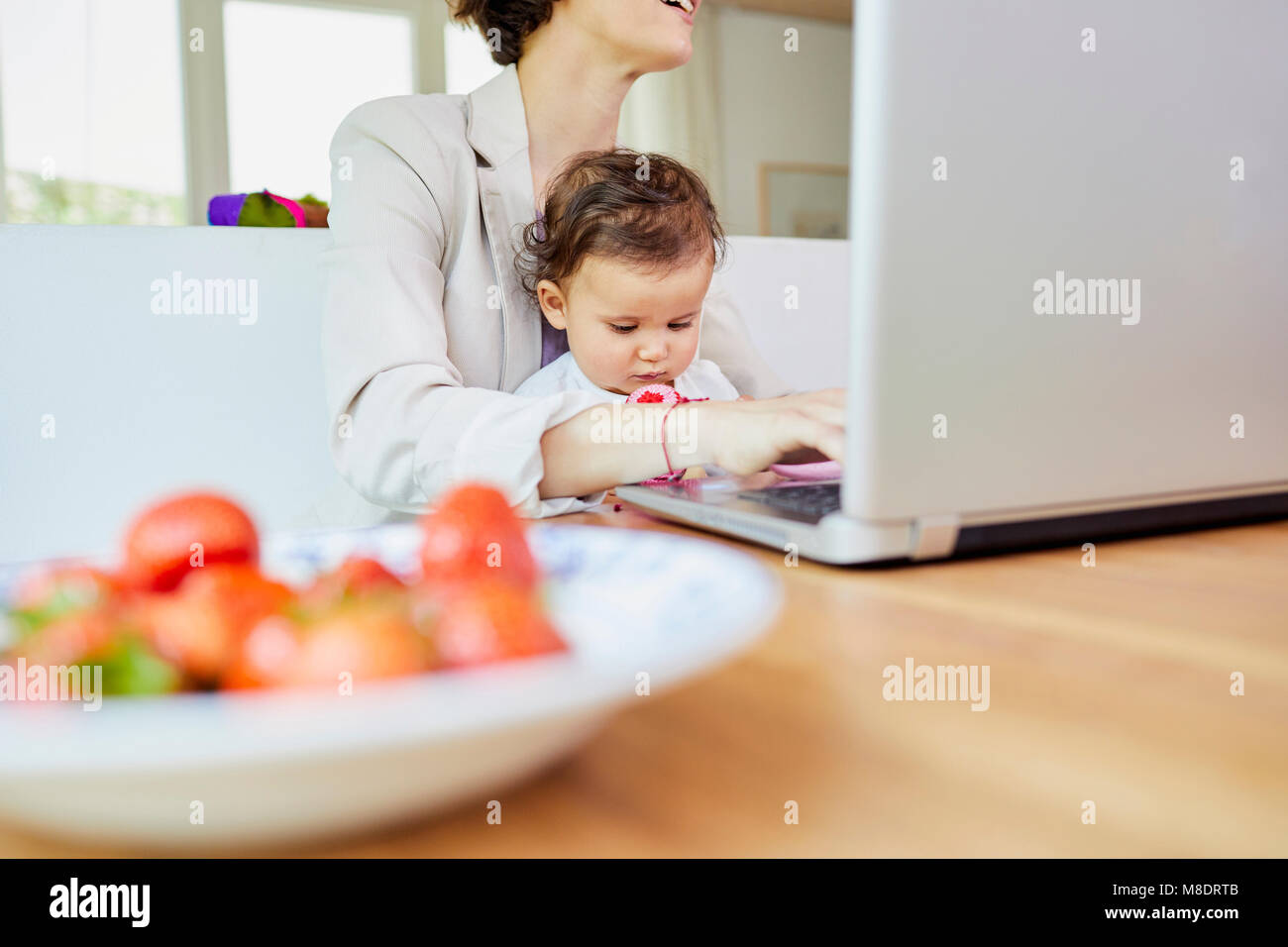 Madre utilizzando laptop con baby ragazza seduta sul suo giro Foto Stock