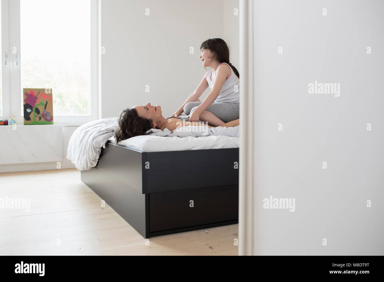 Madre e figlia ingannare intorno in camera da letto, figlia seduta su madre al torace Foto Stock
