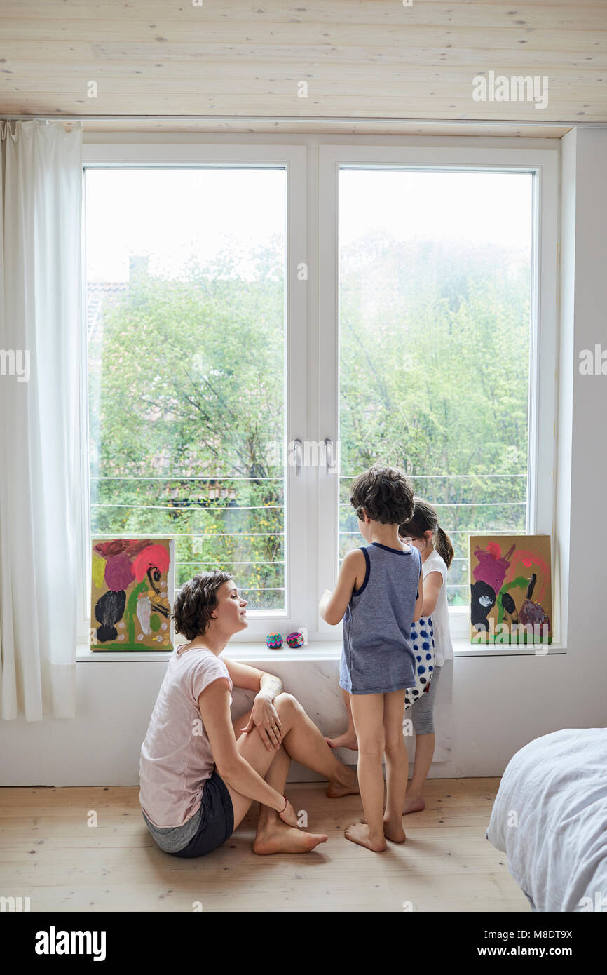 Madre seduta accanto alla finestra, parlando con il figlio e la figlia Foto Stock