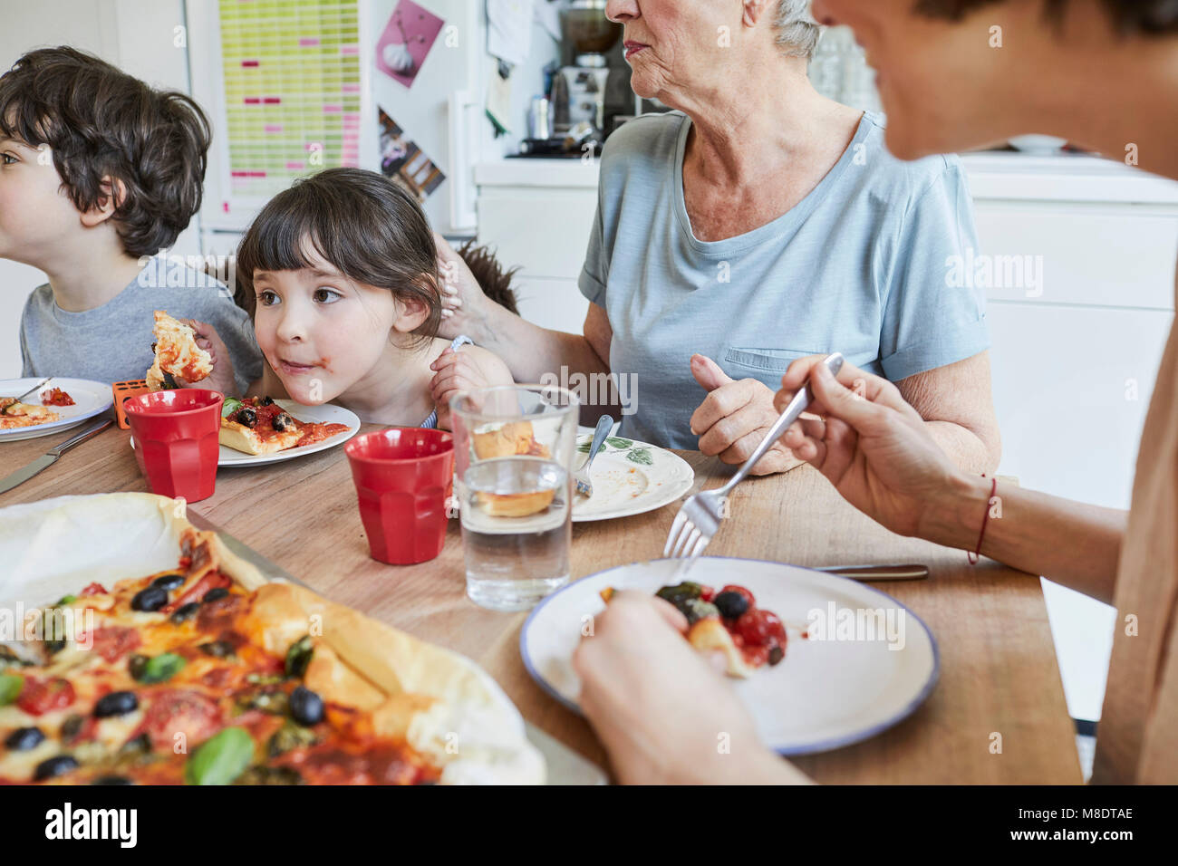 Tre generazioni la famiglia seduta al tavolo della cucina mangiare la pizza Foto Stock