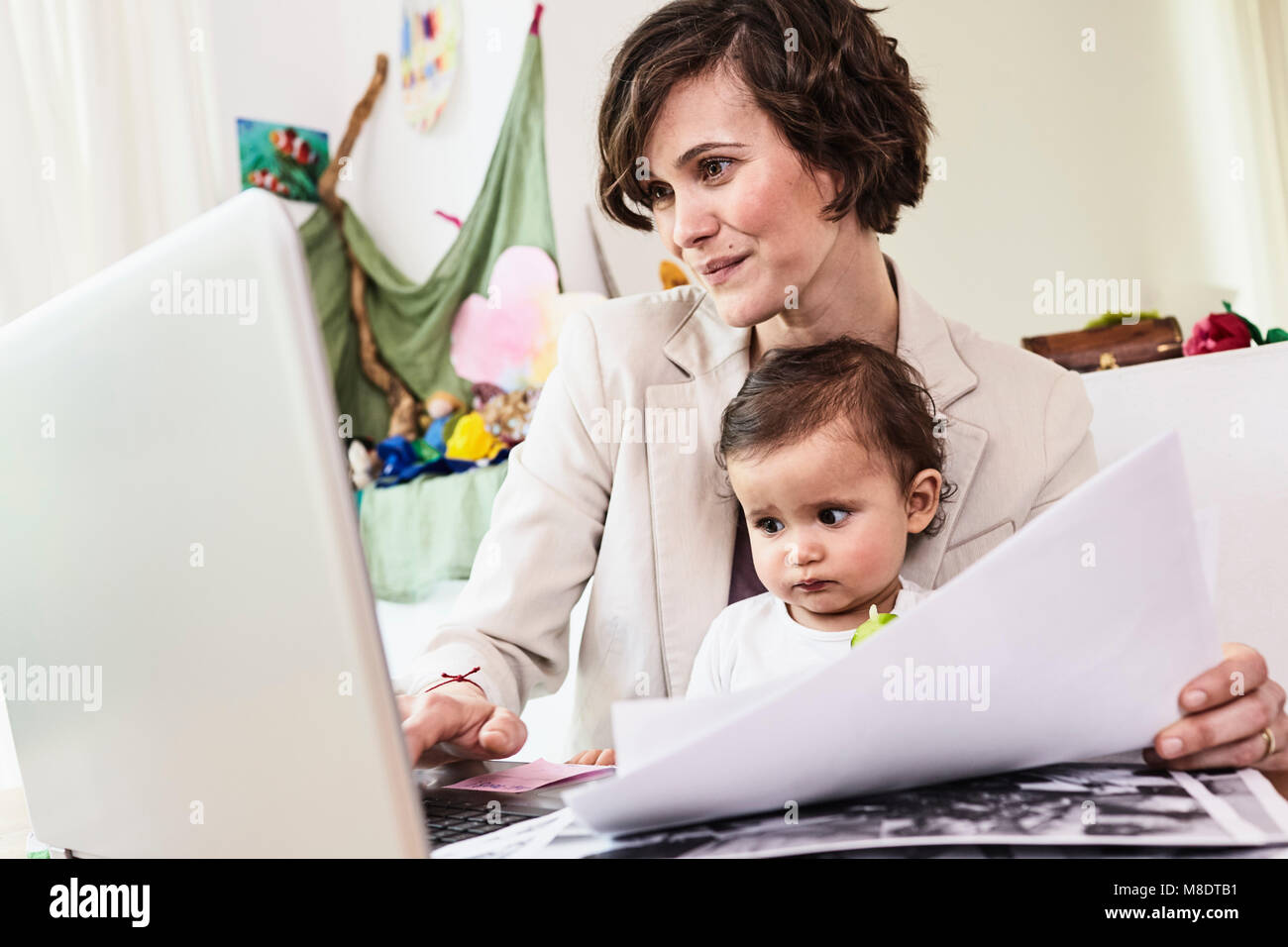 Azienda madre seduta con la nostra bambina, lavorando sul computer portatile Foto Stock