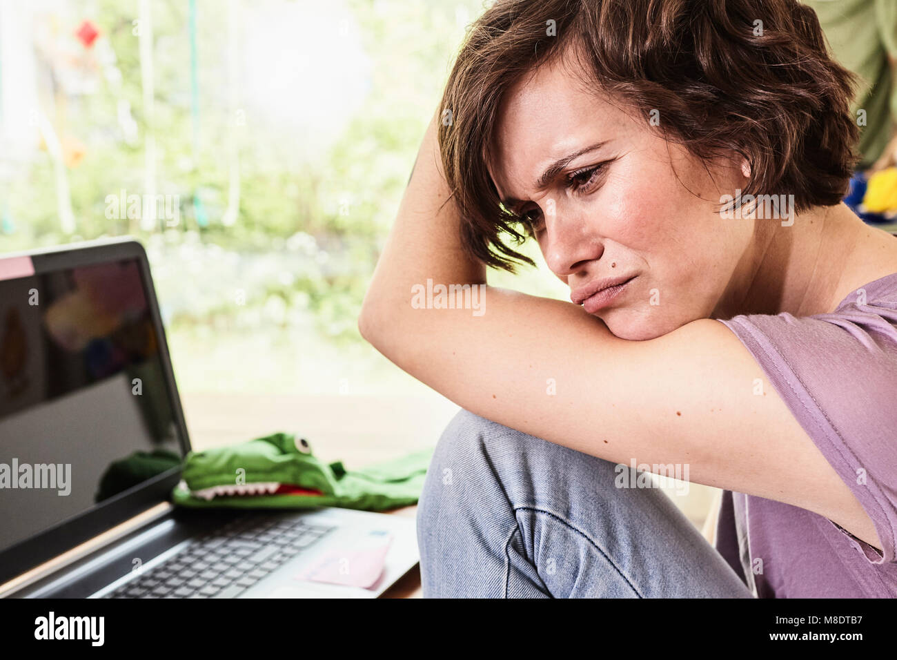 Metà donna adulta a casa, utilizzando laptop, espressione preoccupata Foto Stock