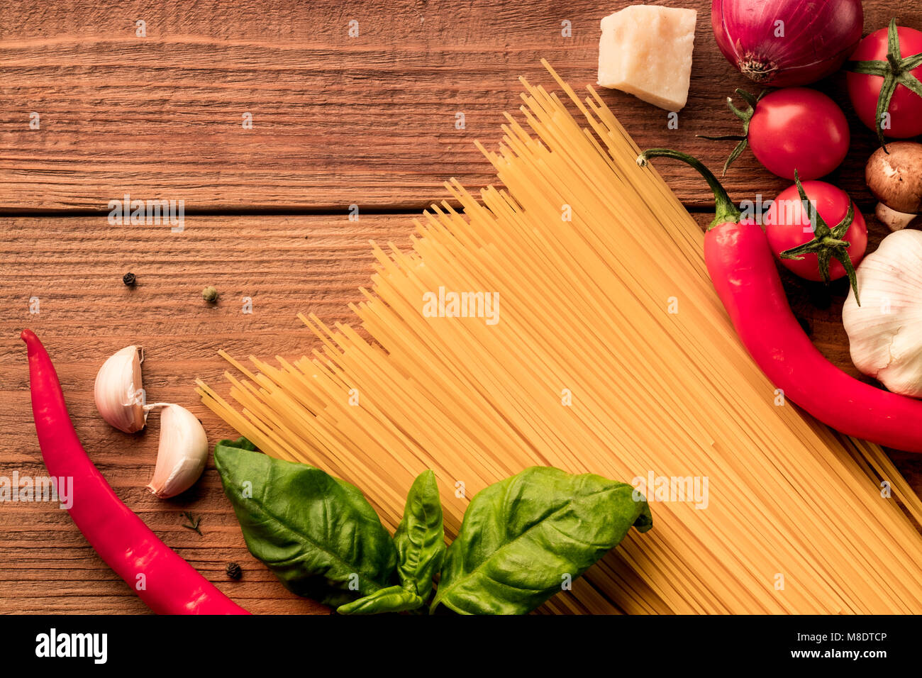 Italian pasta secca spaghetti linguini sparse con pomodori freschi di ciliegia, pepe rosso piccante e il verde del basilico foglie su sfondo di legno. Vista dall'alto. Co Foto Stock