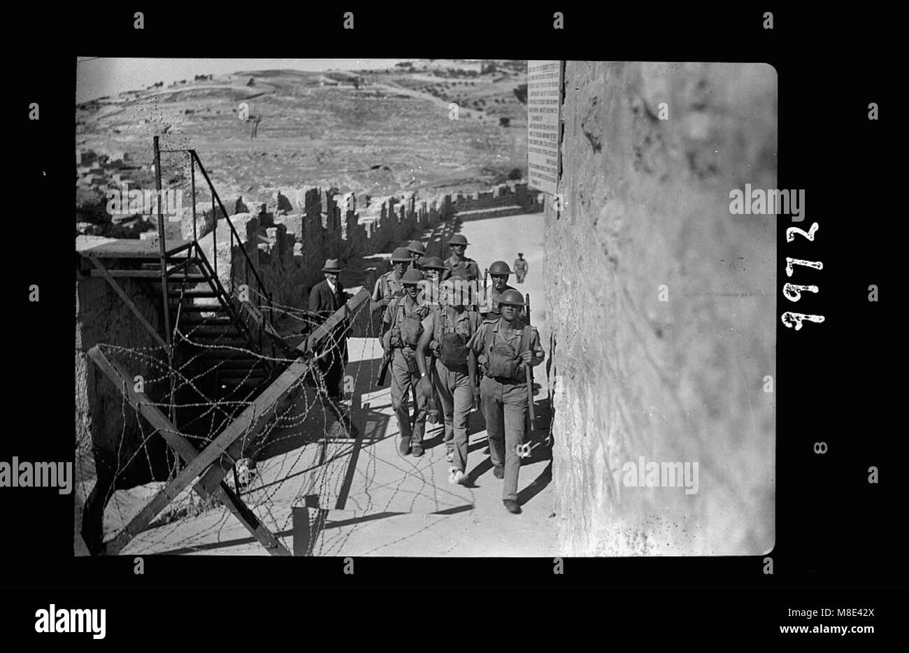 Un'immagine storica che mostra le truppe nella città vecchia di Gerusalemme prima della revoca dell'assedio e del coprifuoco. La foto raffigura soldati in caschi d'acciaio che si innalzano sulle mura della città, sottolineando la presenza militare e la tensione del tempo. Foto Stock