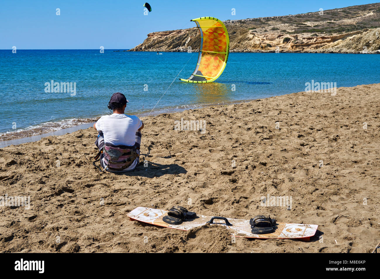 Kitesurfer con paracadute giallo e bordo si siede sulla tranquilla spiaggia di sabbia dell'oceano contro il cielo limpido nella vista posteriore del giorno d'estate Foto Stock