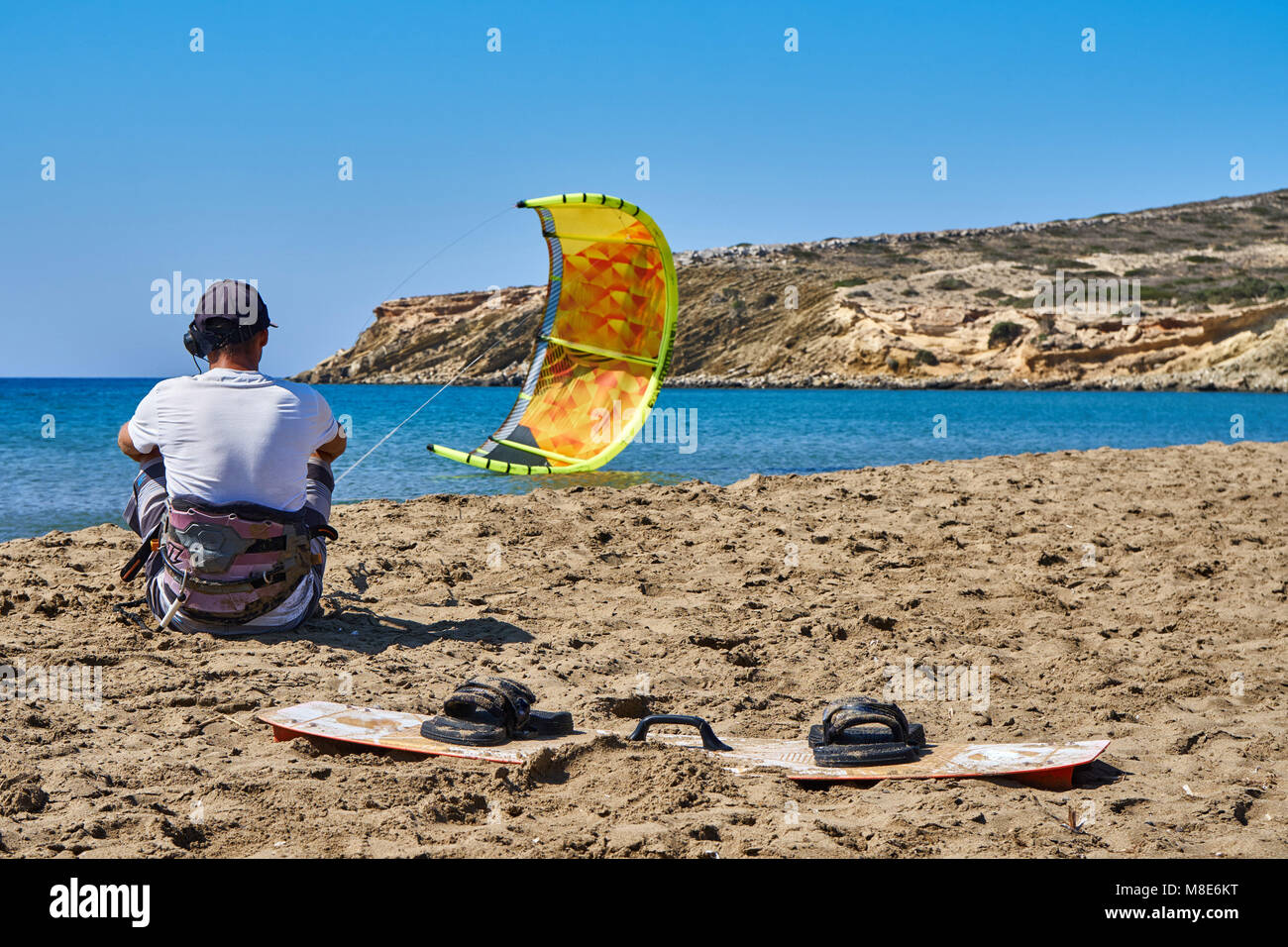 Kitesurfer con paracadute giallo e bordo si siede sulla tranquilla spiaggia di sabbia dell'oceano contro il cielo limpido nella vista posteriore del giorno d'estate Foto Stock