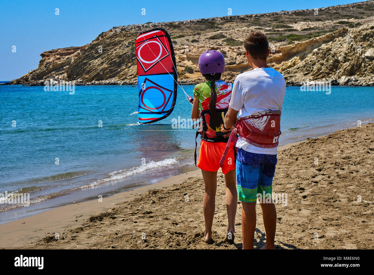 L'istruttore insegna alla giovane donna di andare kitesurf sulla tranquilla spiaggia dell'oceano contro il cielo limpido sulla soleggiata vista sul retro del giorno d'estate Foto Stock