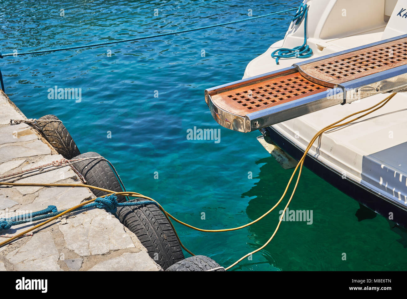 Scala d'imbarco di barca a motore bianco lucido di design moderno ormeggiata al molo con corde sull'acqua di mare blu che riflette la luce del sole luminoso il giorno d'estate Foto Stock