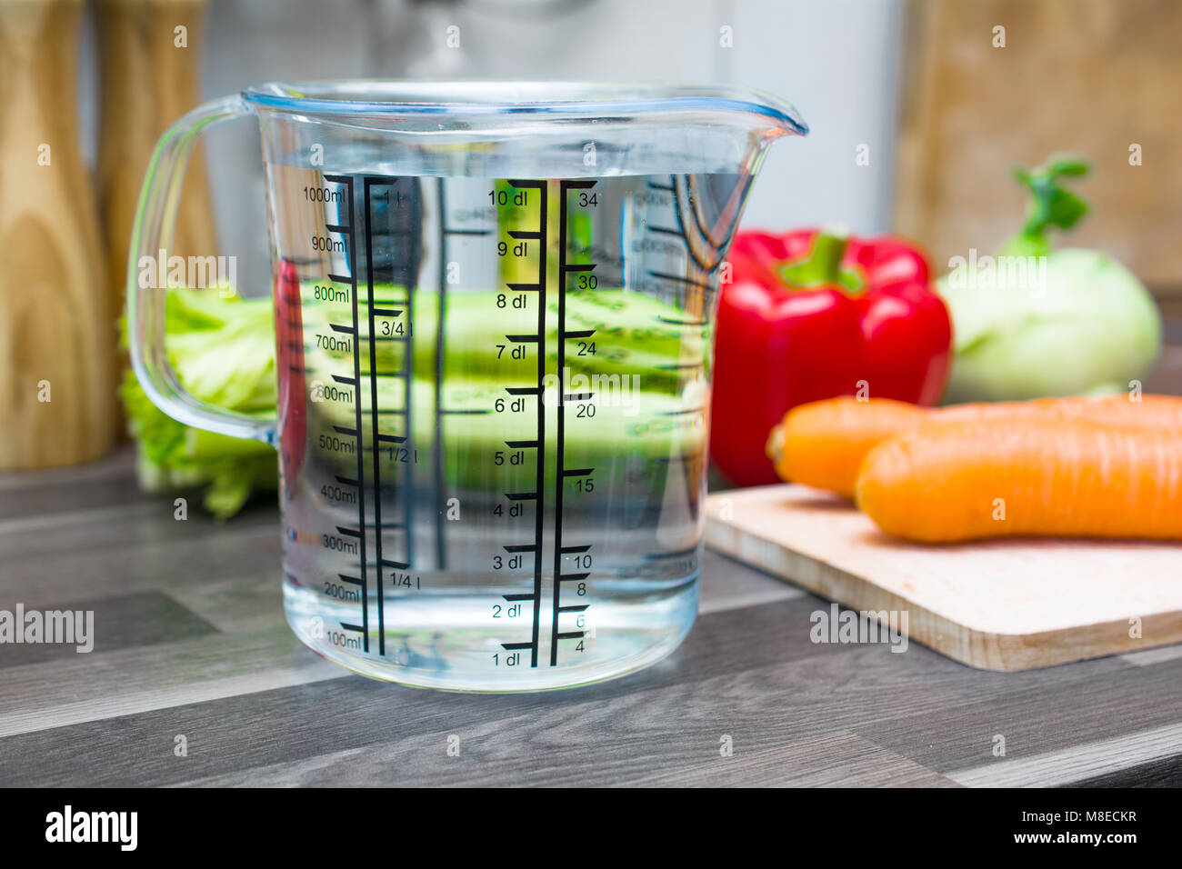 1 litro / 1000ml / 10dl di acqua in una coppa di misurazione su un bancone cucina con verdure Foto Stock