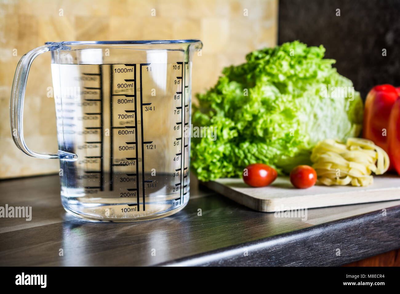 1000ccm / 1 litro / 1000ml di acqua in una coppa di misurazione su un banco di cucina con i prodotti alimentari Foto Stock