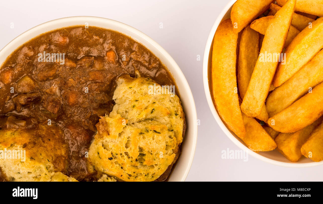 Tradizionali di carni bovine britanniche casseruola con canederli contro un fondo azzurro e una ciotola di patatine o patate fritte Foto Stock