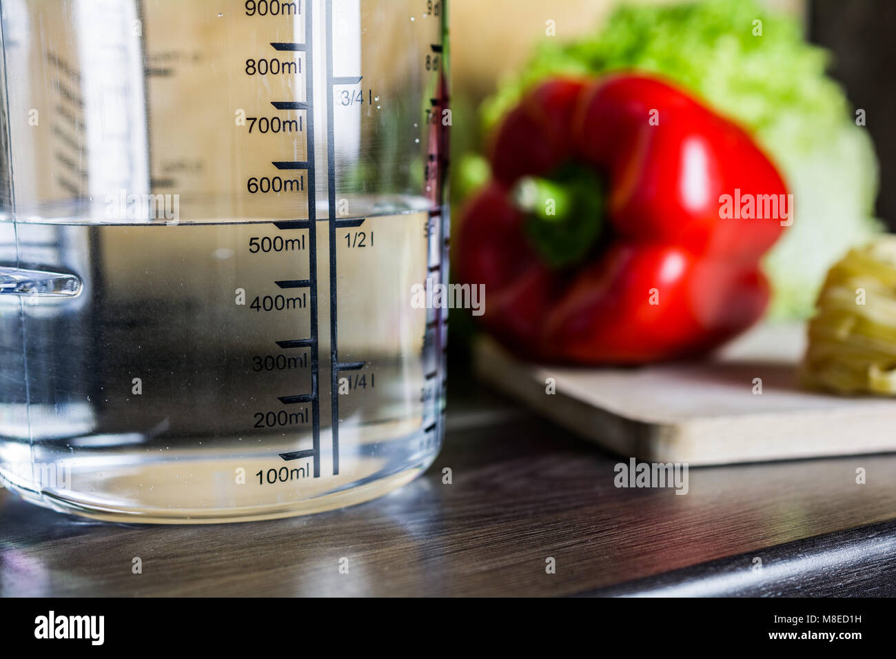 500ccm / 1/2 litro / 500ml di acqua in una coppa di misurazione su un banco di cucina con i prodotti alimentari Foto Stock