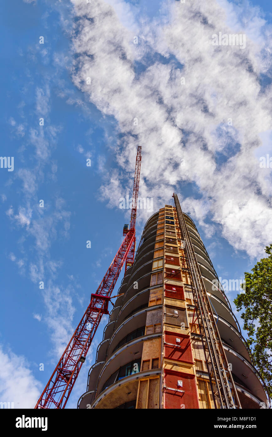 Vista dal basso verso l'alto sulla costruzione di una gru a torre, un edificio a più piani in un giorno di estate contro un cielo blu e nuvole bianche Foto Stock